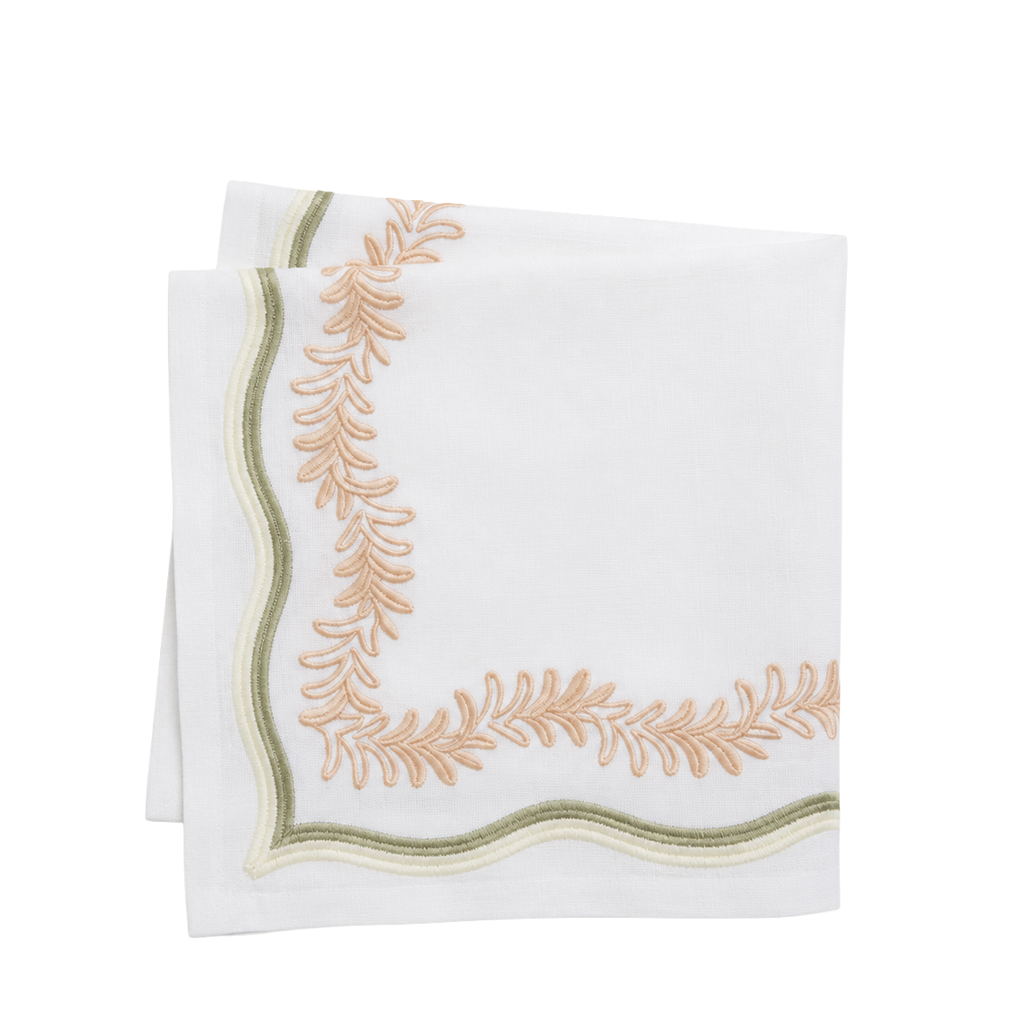 A folded white linen napkin with scalloped edges and embroidered leafy corner details in peach and olive green.