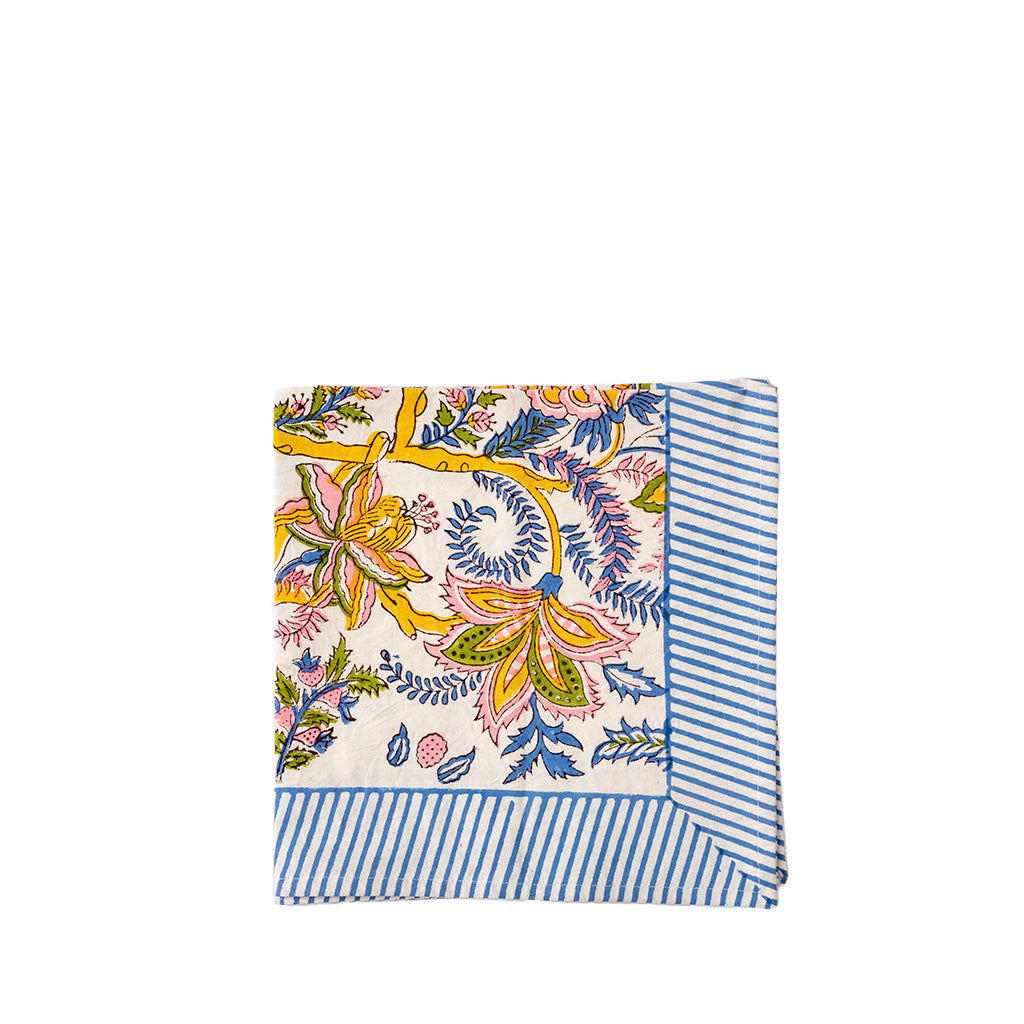A folded napkin with a multicolor floral block print on a cream background and blue-and-white striped borders, displayed on a plain white background.