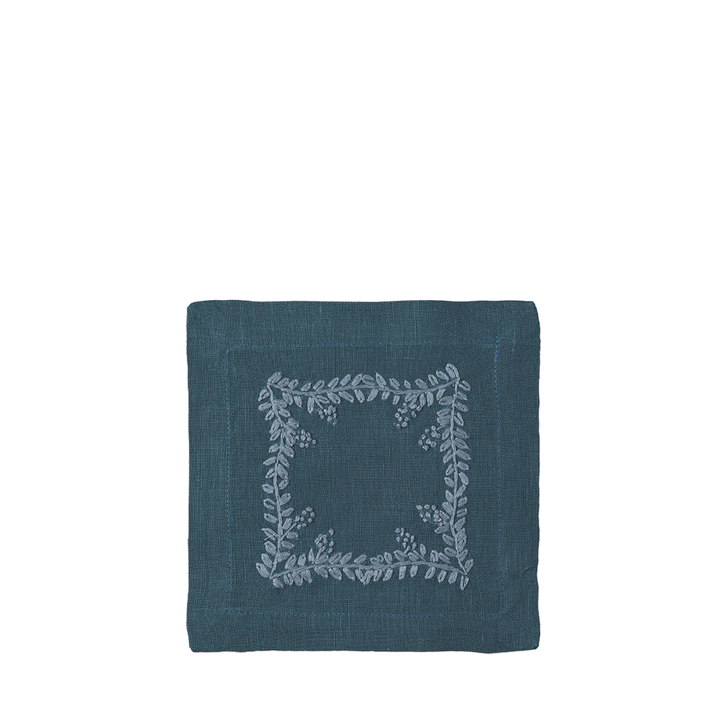 A square dark teal linen napkin featuring a light gray embroidered floral wreath border in the center, presented on a solid white background.