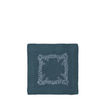 A square dark teal linen napkin featuring a light gray embroidered floral wreath border in the center, presented on a solid white background.