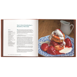 Open cookbook showing a recipe for strawberry shortcake with a stack of strawberries and whipped cream on a plate.
