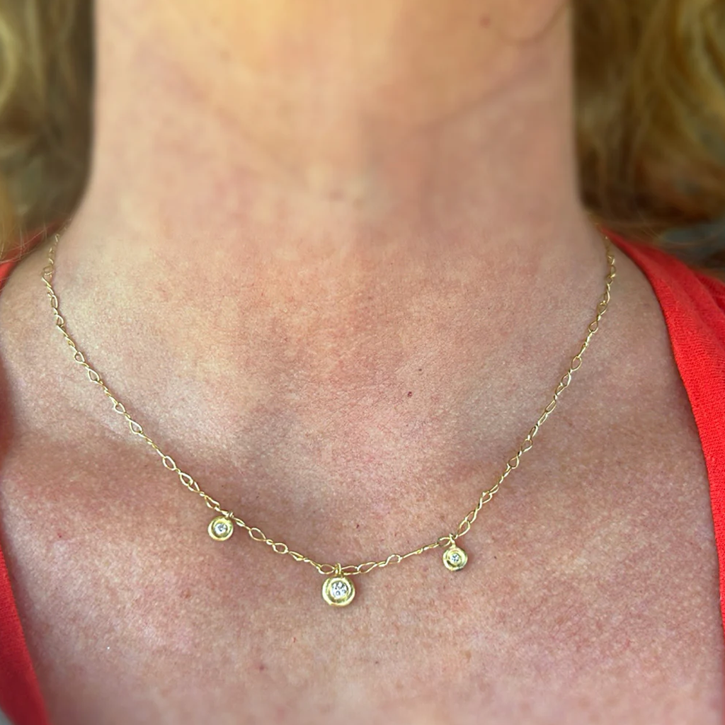 Gold necklace with small round pendants on a person wearing a red top.