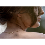 Close-up of a person wearing a delicate gold necklace with a blurred background
