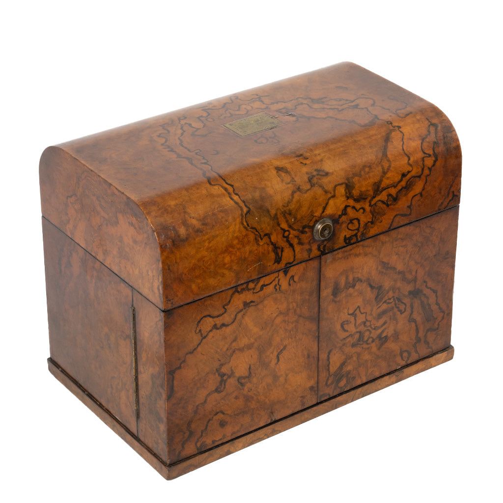 A vintage wooden chest with a hinged lid, featuring rich burl wood grain patterns in warm brown and amber tones, secured with a small metal snap button on the front.