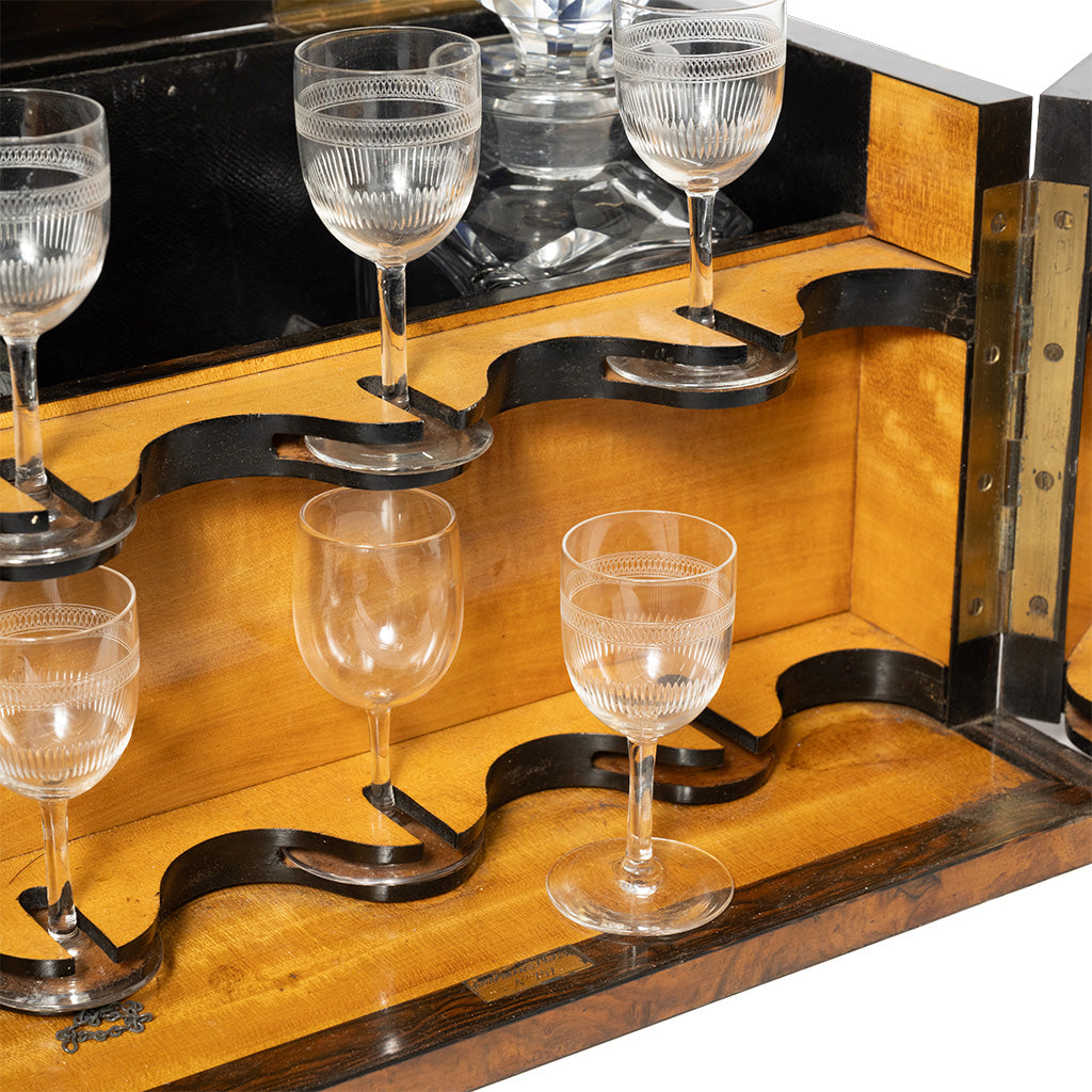 The interior of an open wooden liquor box features fitted holders displaying several etched stemmed glasses, with a mirrored back reflecting the glassware. The warm wood lining and custom compartments are designed to securely store and organize the matching drinkware.