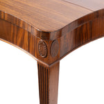 Close-up of a polished wooden table corner with a fluted leg and carved circular medallions on the apron, shown against a white background.
