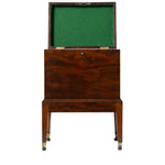 A front view of an antique mahogany cellaret with its hinged lid open reveals a green felt-lined interior designed for storing bottles. The piece stands on straight legs with brass-capped feet and features a simple, elegant design with a central keyhole on the front.