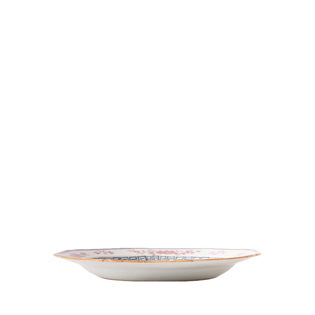 Side view of a shallow decorative ceramic plate with a gently flared rim, finished with a thin gold edge. The interior features soft pink floral motifs and a blue geometric border, while the white exterior has a smooth, simple profile.