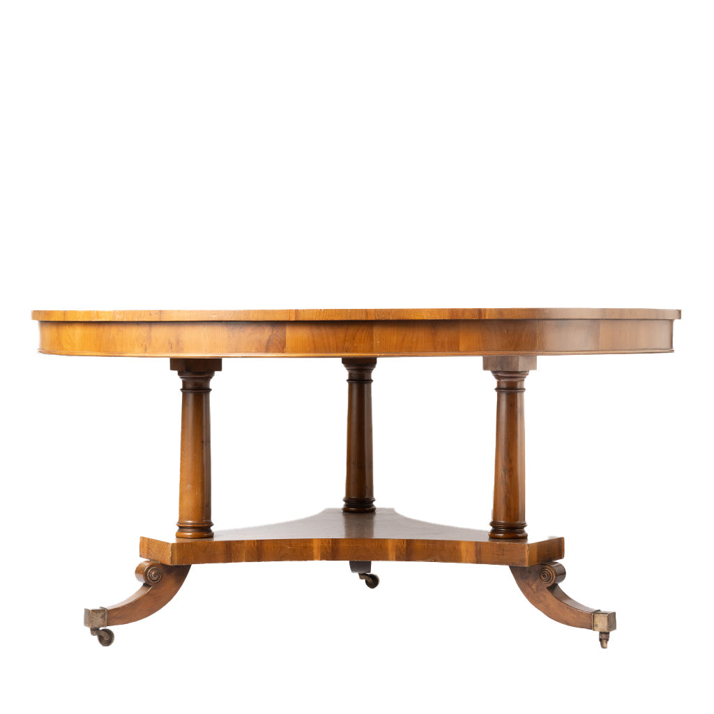 A round wooden table with turned pedestal legs and curved feet on casters, shown against a plain white background.