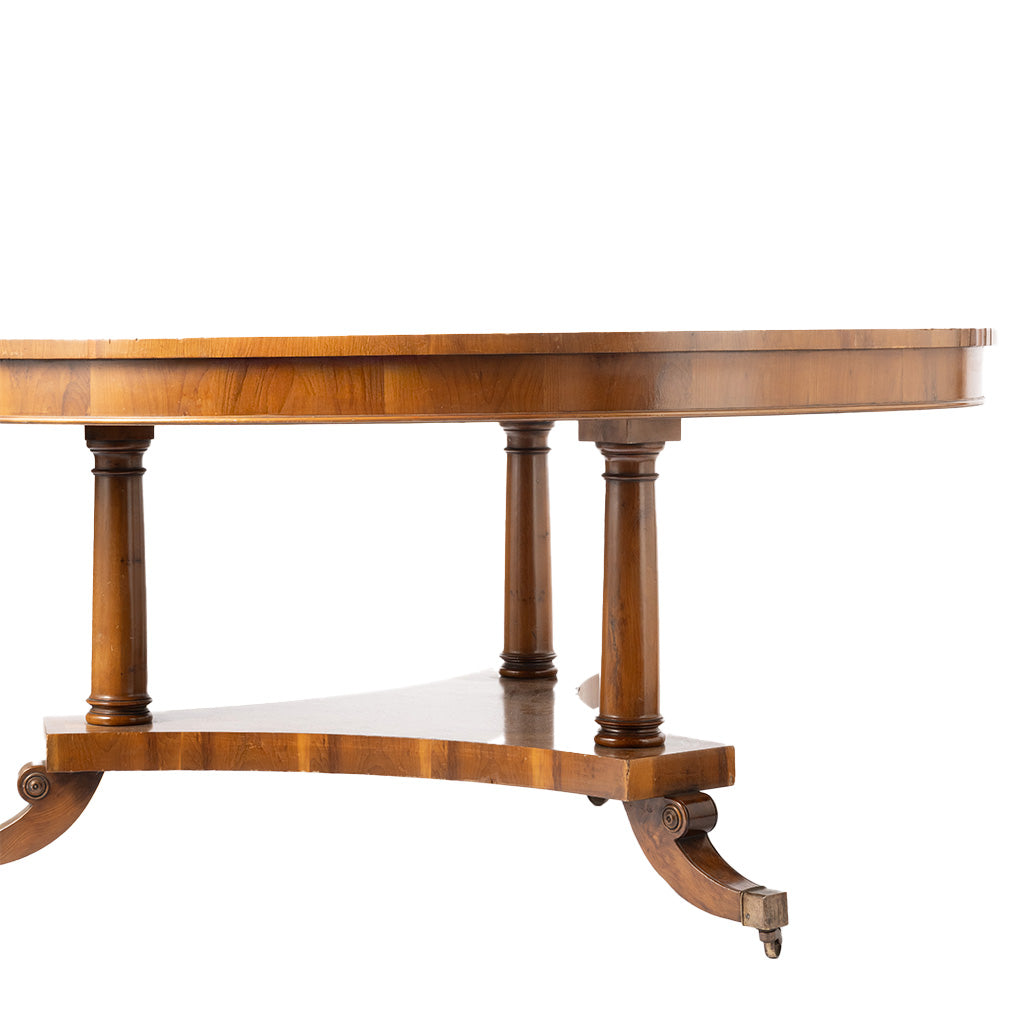 A close-up of a round wooden dining table featuring turned legs and a curved apron, shown against a plain white background.