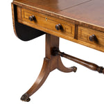 Close-up of an antique wooden writing desk with three drawers, decorative drawer pulls, a drop-leaf design, and a turned pedestal leg on a white background.