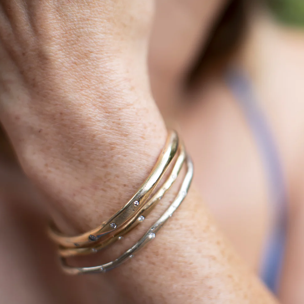 Close-up of a wrist wearing multiple gold bracelets with a blurred background