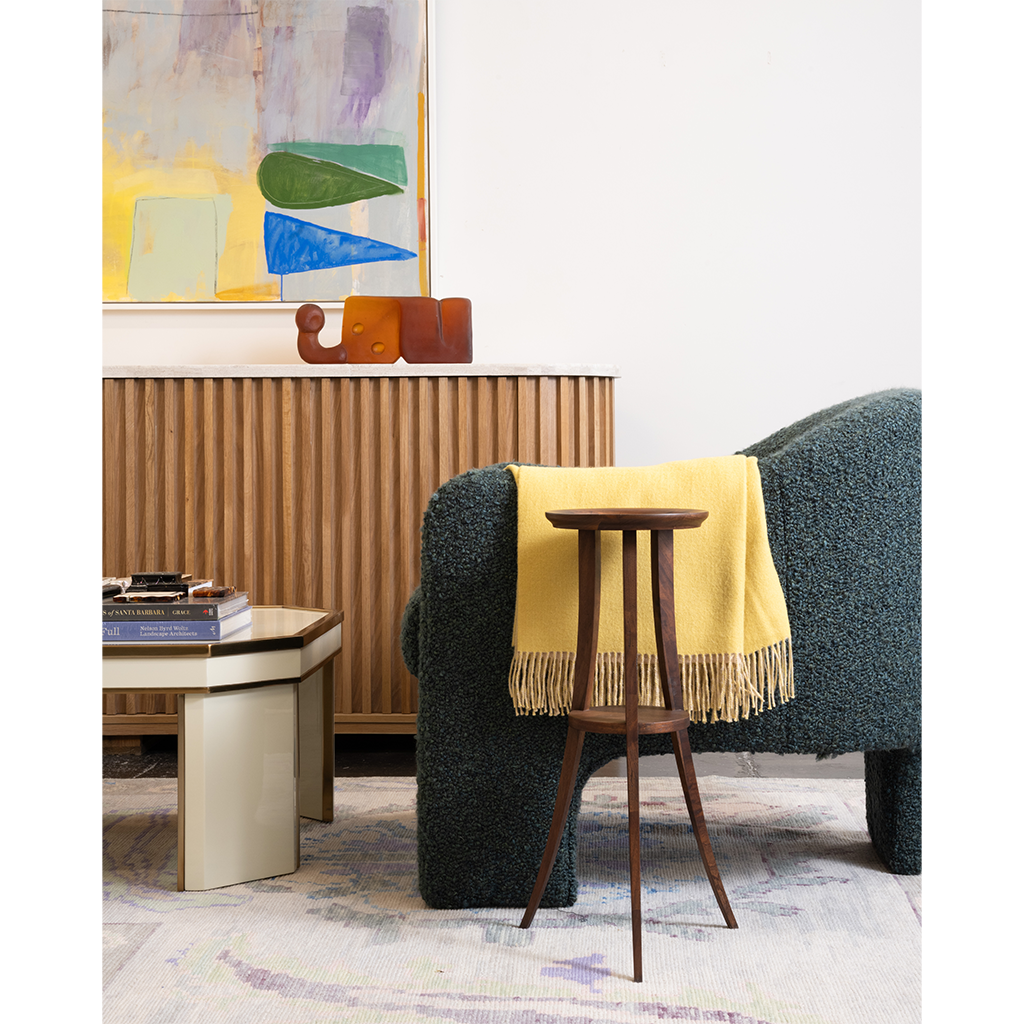A dark blue chair with and wooden side table with artwork in the background