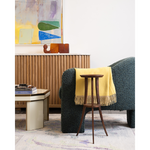 A dark blue chair with and wooden side table with artwork in the background