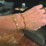 Close-up of a wrist wearing two gold bracelets with a blurred indoor background