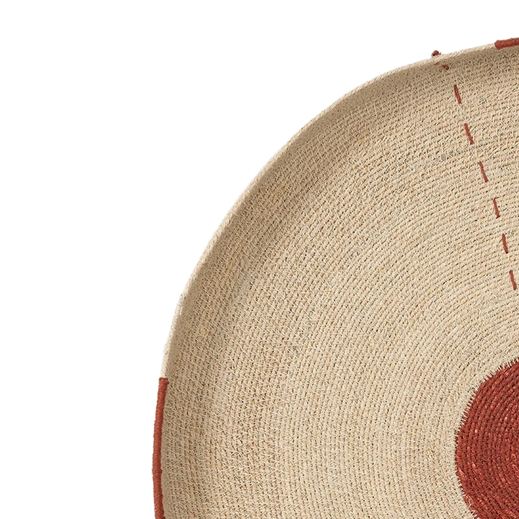 Close-up detail of a woven natural fiber product, showing a beige textured surface with red stitched accents and a partial red circular motif on a white background.