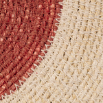 Close-up of a woven textile surface with two main color fields: a rust red section on the left and an off-white/cream section on the right, both showing a braided or knotted texture.