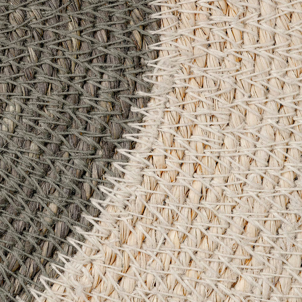 Close-up of a woven textile surface showing two main color fields: a dark gray section on the left and a warm off-white/cream section on the right, with diagonal textured yarns crossing the whole frame.