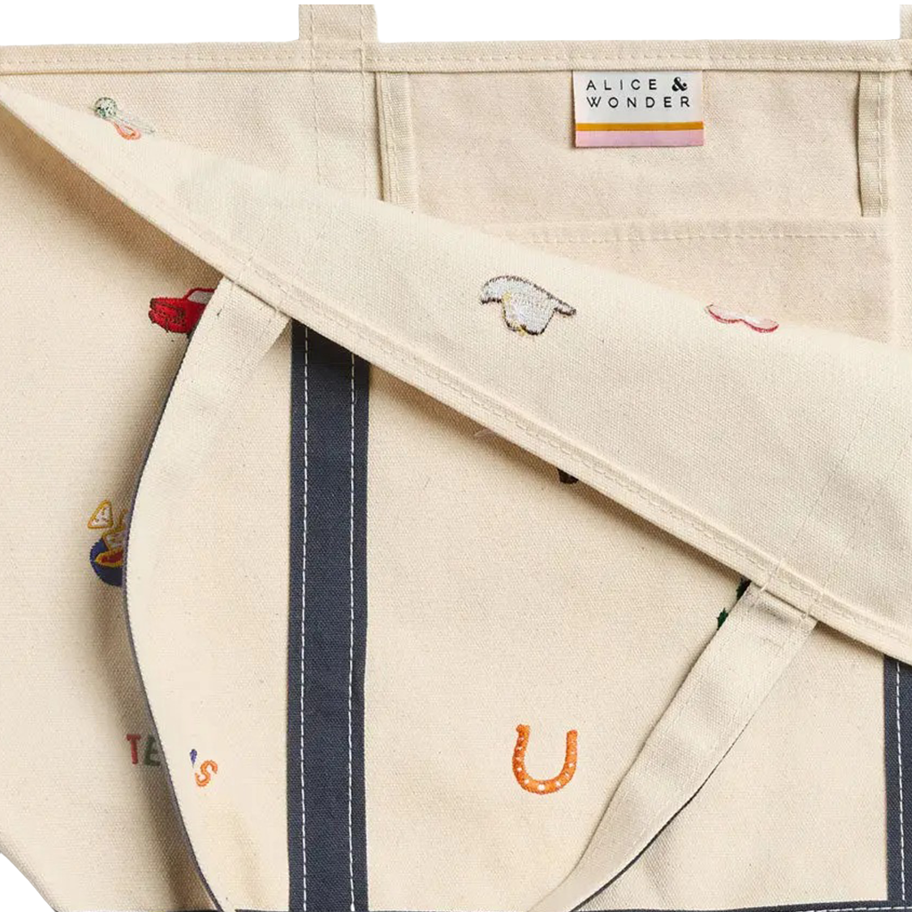 Close-up of a canvas tote bag in warm off-white/cream with embroidered motifs including a sheep, a red car, and small colorful details. A sewn label at the top reads ALICE & WONDER.