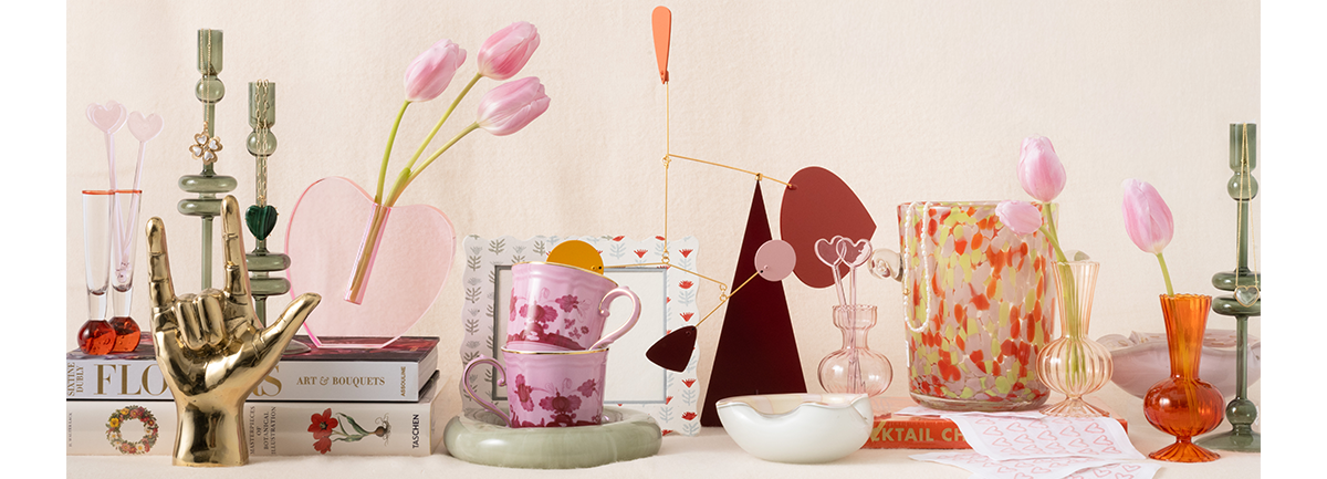 Decorative items including a pink mug, candlesticks, and vases on a white surface with a light pink background.