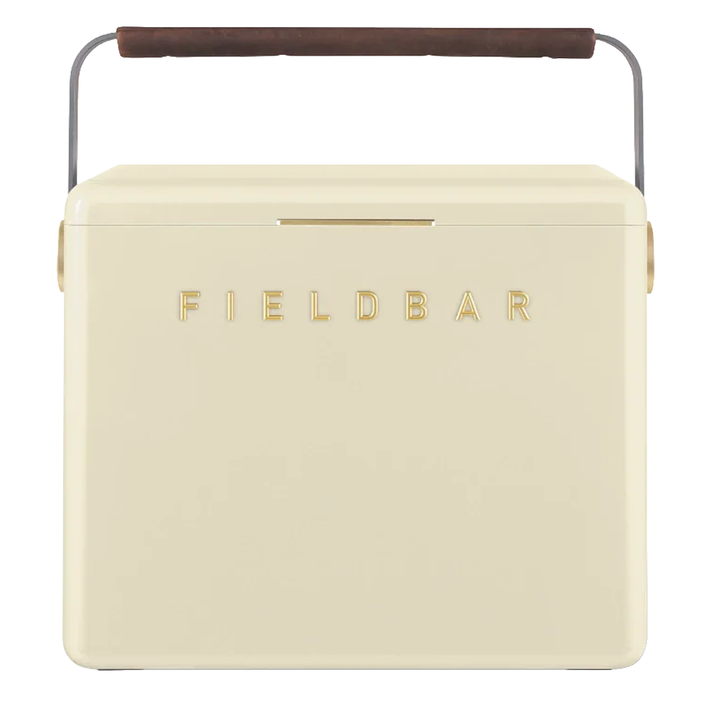 A cream FIELDBAR cooler with gold lettering, rounded edges, and a slim gold latch is shown against a white background. It features a curved metal handle wrapped with a brown leather grip, giving it a modern, premium appearance.