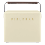 A cream FIELDBAR cooler with gold lettering, rounded edges, and a slim gold latch is shown against a white background. It features a curved metal handle wrapped with a brown leather grip, giving it a modern, premium appearance.