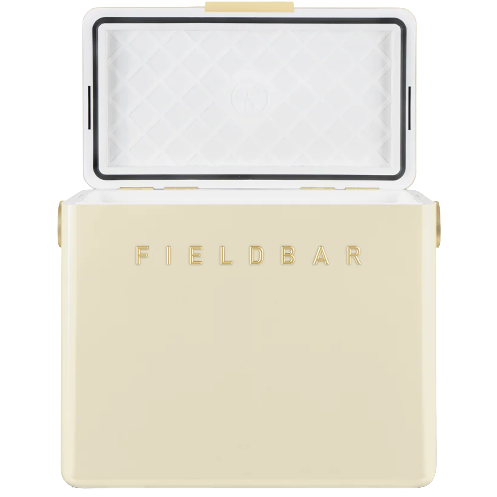 The cream FIELDBAR cooler is shown with its lid open, revealing a white insulated interior with a quilted pattern and a black sealing gasket around the edge. Gold lettering on the front and gold hardware accents complement the cooler's clean, premium design against a white background.