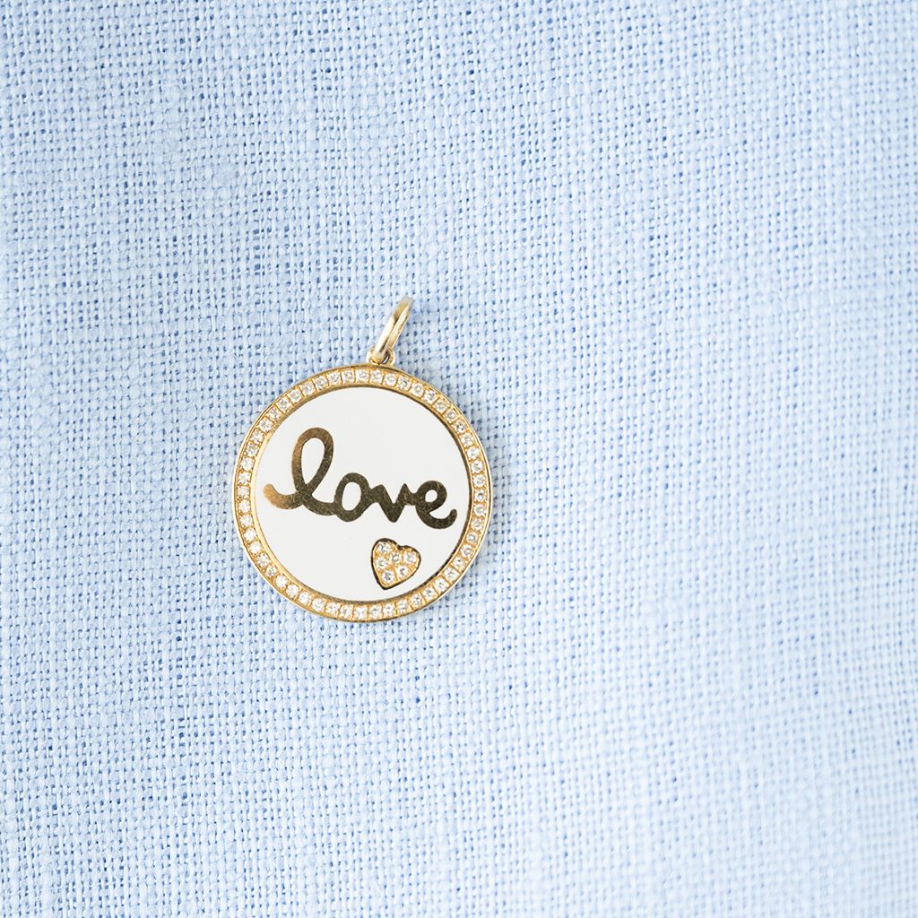 Round pendant with 'love' engraving on a light blue fabric background