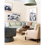 A styled living room featuring a striped green and beige sofa, a dark gray swivel chair, a beige armchair, a wooden coffee table, and three framed black-and-white art prints on a textured beige wall.