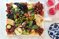 White Rectangular Charcuterie Board filled with cheese, grapes, honey, and other accoutrements 