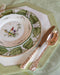 Side view of Christofle Jardin D'Eden Flatware displayed with accent plate, dinner plate and placemat on top of tablecloth